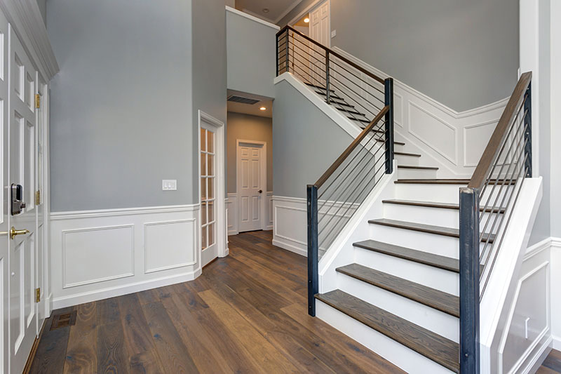 Home 211 A modern home entryway with light gray walls, white trim, dark wood flooring, and a staircase with dark wood steps and black metal railings, leading to an upper hallway. Multiple white doors are visible.
