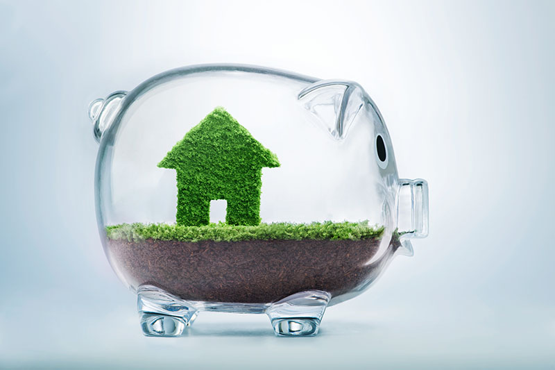 Home 219 A transparent piggy bank contains soil and a small green house figure made of grass, symbolizing saving money for a home or eco-friendly housing investments.
