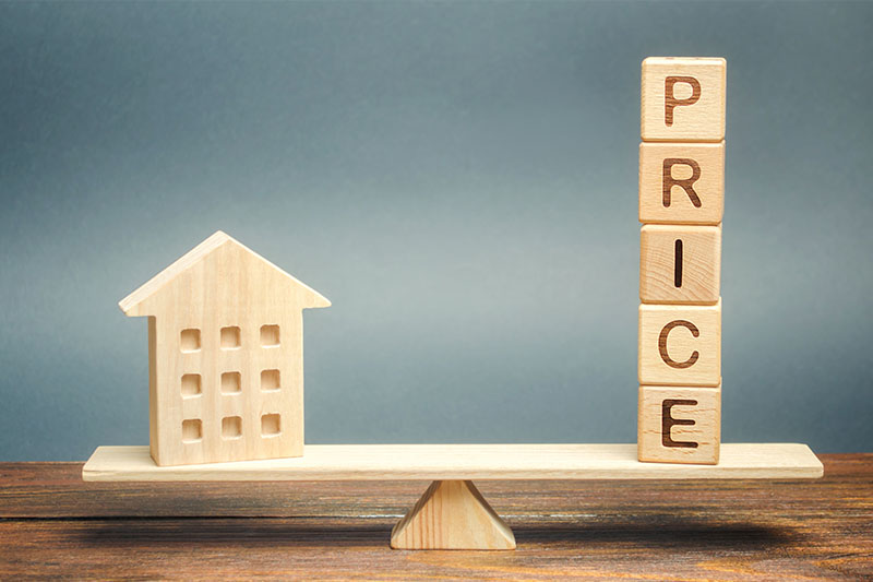 Home 222 A wooden house model and stacked blocks spelling PRICE are balanced on a seesaw, symbolizing the relationship between property value and price.