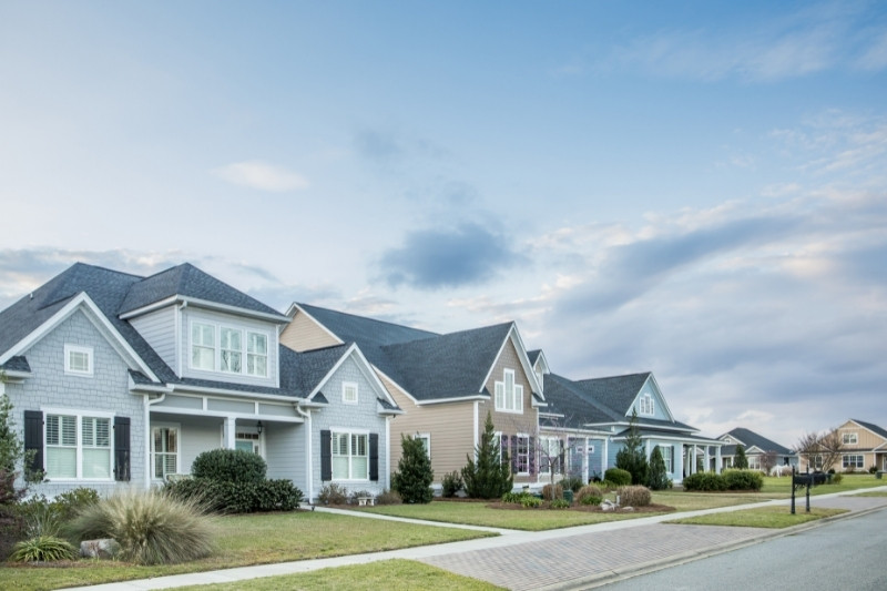 Home 199 A row of modern suburban houses with well-kept lawns and landscaping under a partly cloudy sky, lining a quiet residential street.