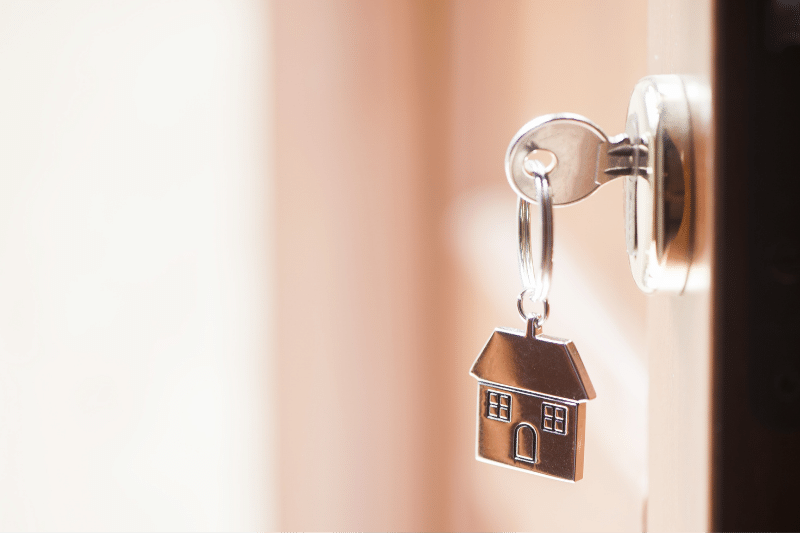 Home 88 A silver key with a house-shaped keychain is inserted into a door lock, with soft natural light shining from the left side of the image.