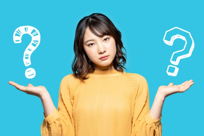 Home 51 A woman in a yellow top stands against a blue background, holding her hands up with a questioning expression. Large white question marks are illustrated near each hand, symbolizing confusion or decision-making.