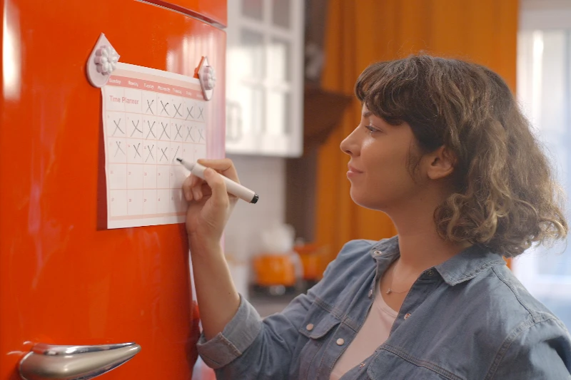 Home 17 Woman marking off her calendar hanging on a fridge