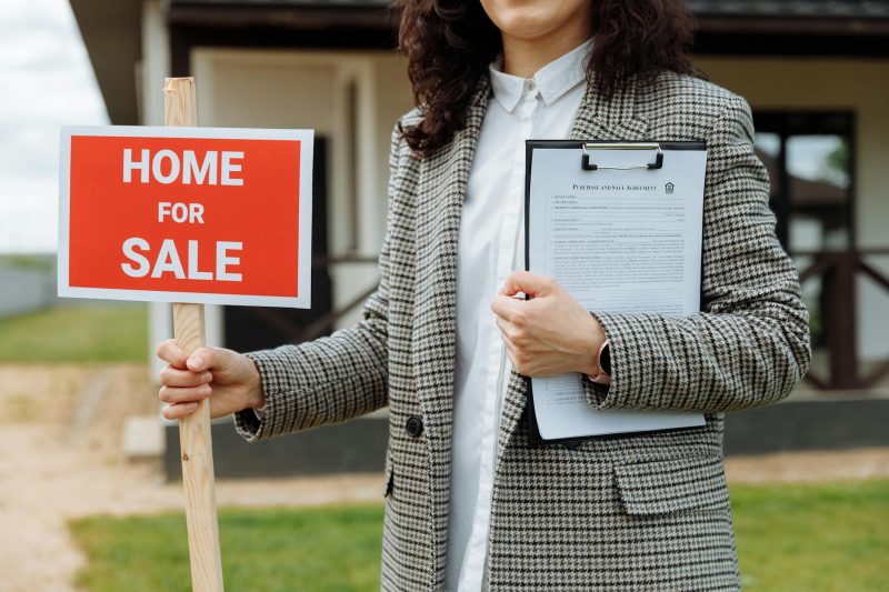 Home 15 A real estate agent holding a home for sale sign and clipboa 1779814844