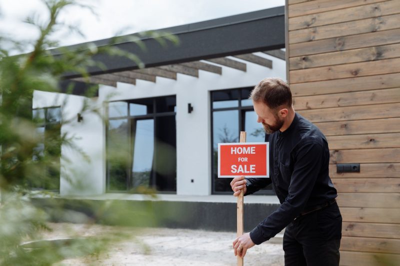 Home 11 Man placing a home for sale sign outside a modern house for 1785862952